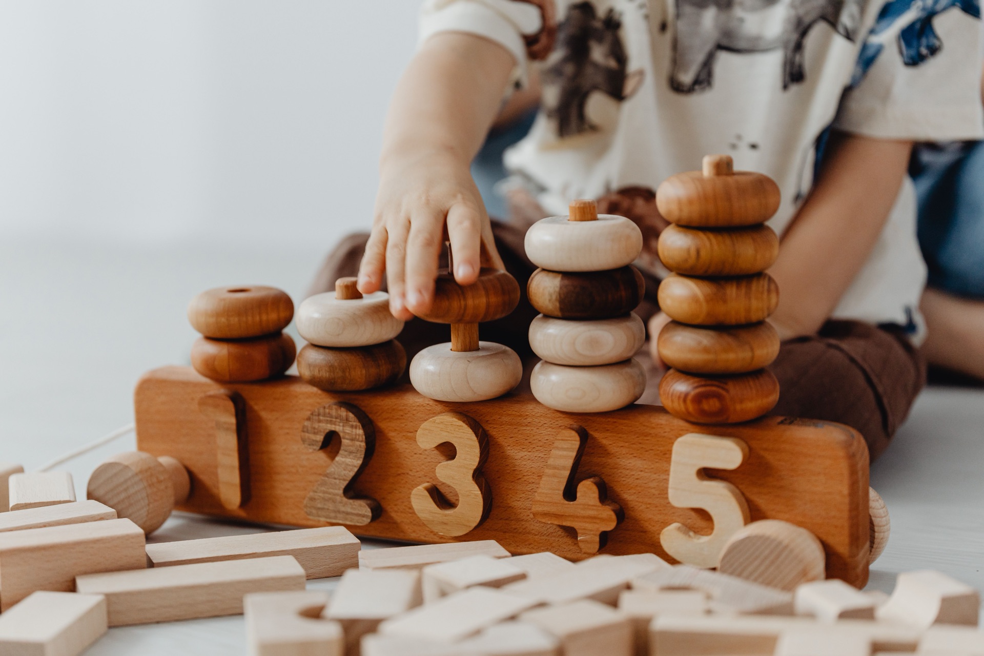 A toddler's hands stacking a warm wooden Montessori counting toy carved with the numbers 1 through 5.