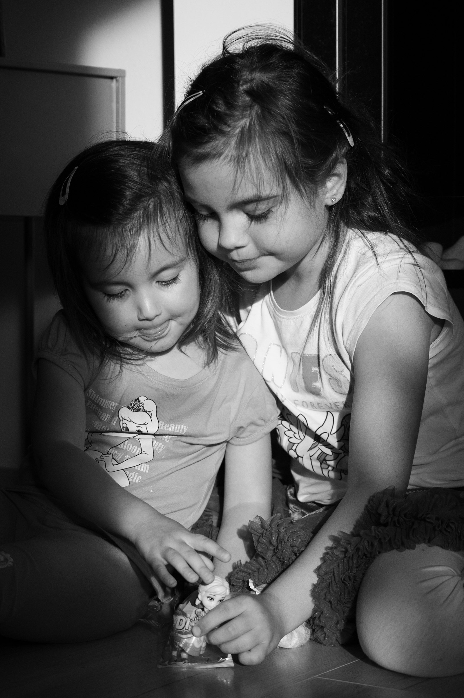 A tender moment of toddlers sitting quietly on a woven rug, gently exploring wooden language toys near soft linen curtains.