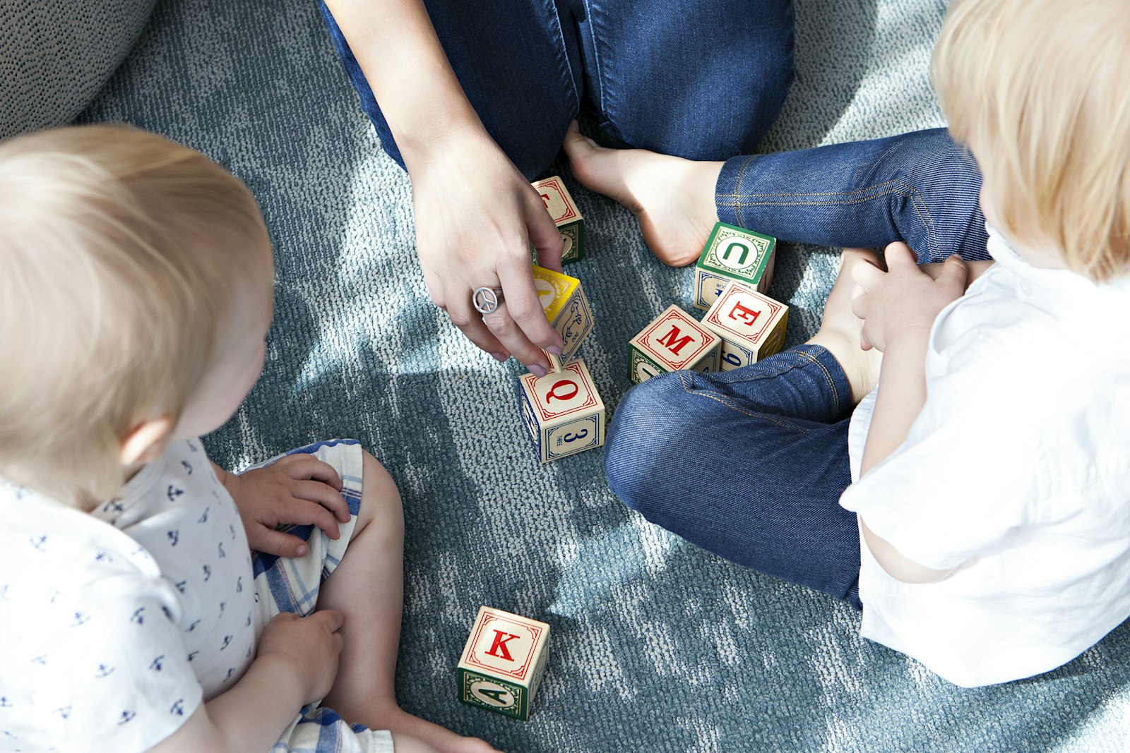 Children gathered around natural wood blocks engraved with letters, bathed in warm golden afternoon light.