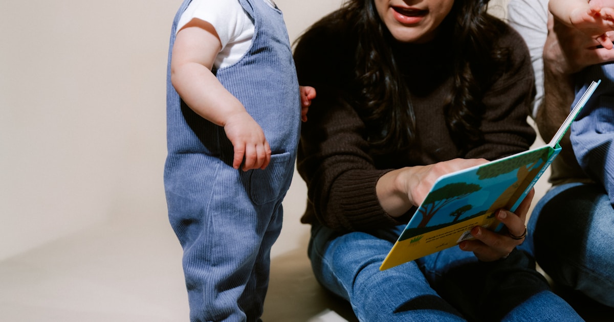 Family reading a book together on a plain background.