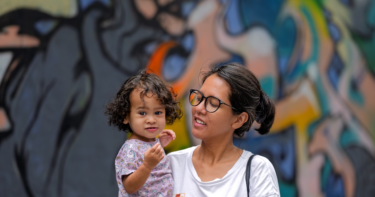 Mother holds her child near colorful street art.