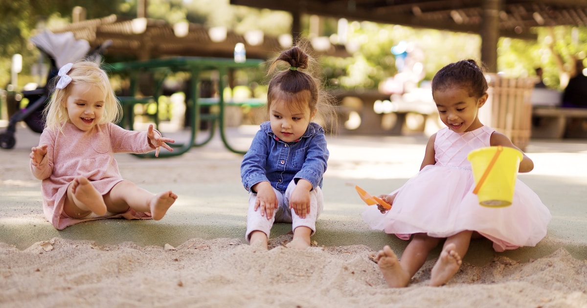 girl in pink dress sitting on brown sand during daytime