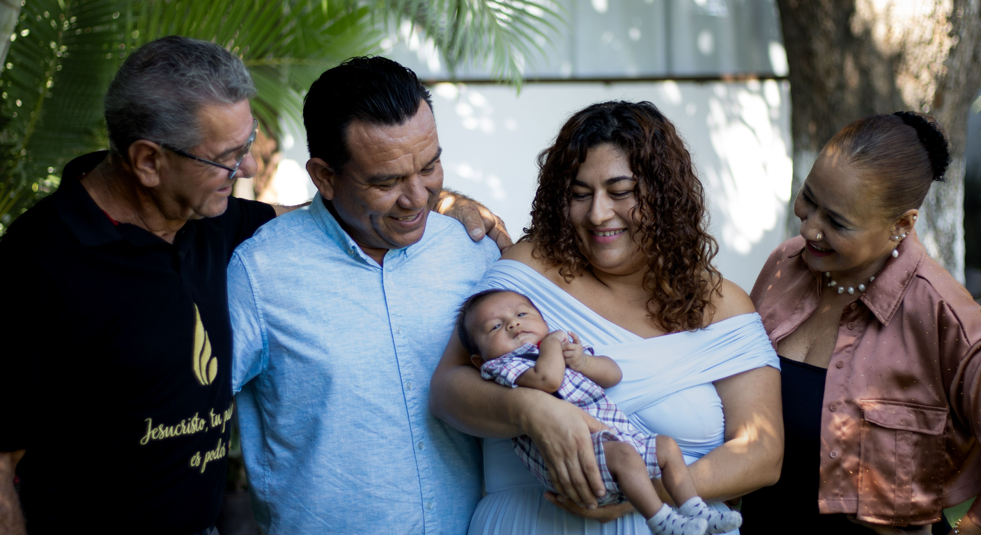 A multigenerational family standing close together, one parent holding a newborn.