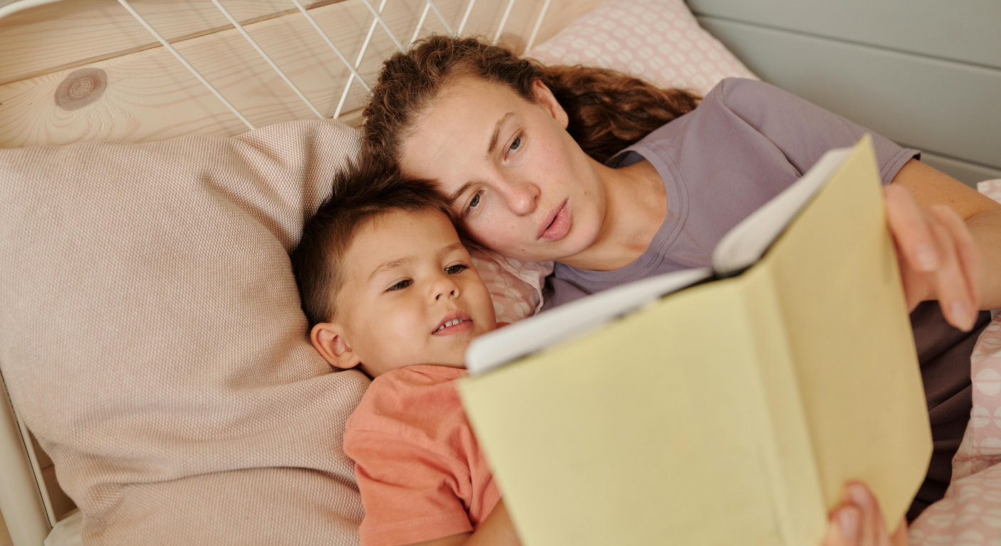 Mother and child reading a picture book together in bed in a cozy bedroom