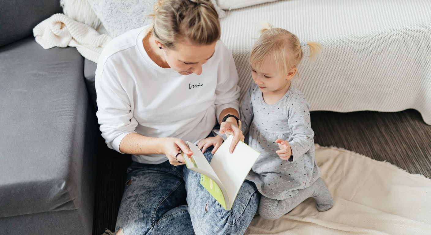 A mother and toddler reading a picture book together on the floor