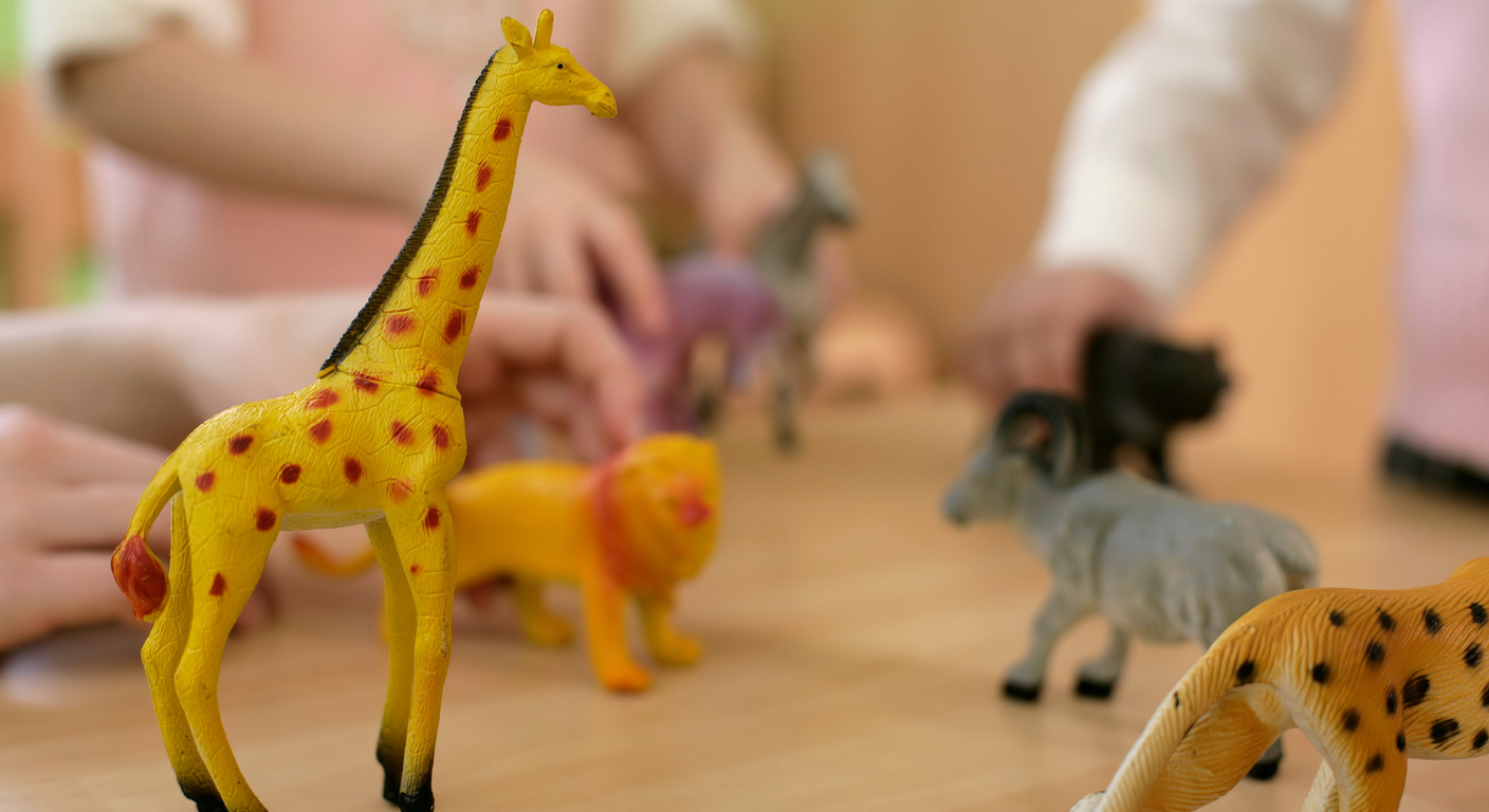 A young child's hands and an adult's hands playing together with plastic animal figures.