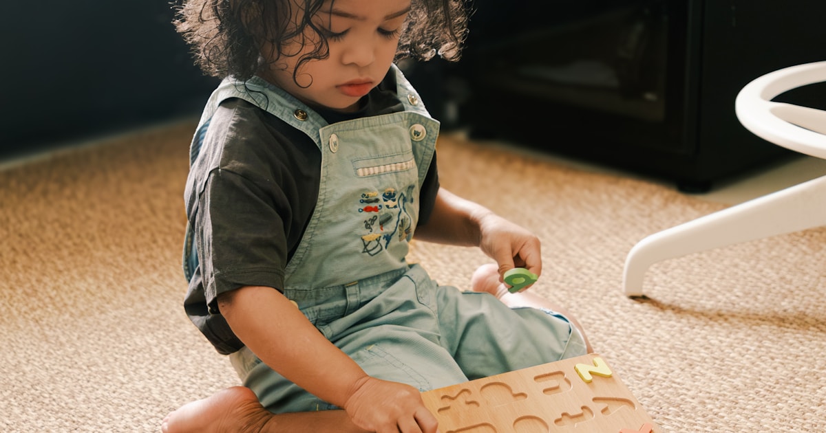 Young child plays with alphabet puzzle on floor.