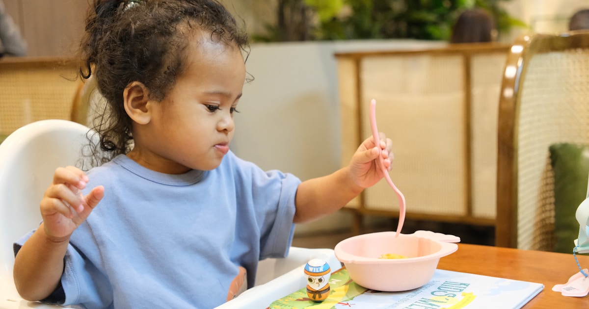 Young child eating with a pink spoon and bowl.