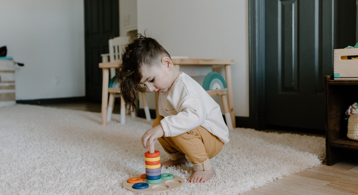 A toddler working with real wooden Montessori materials on a low shelf in warm natural light