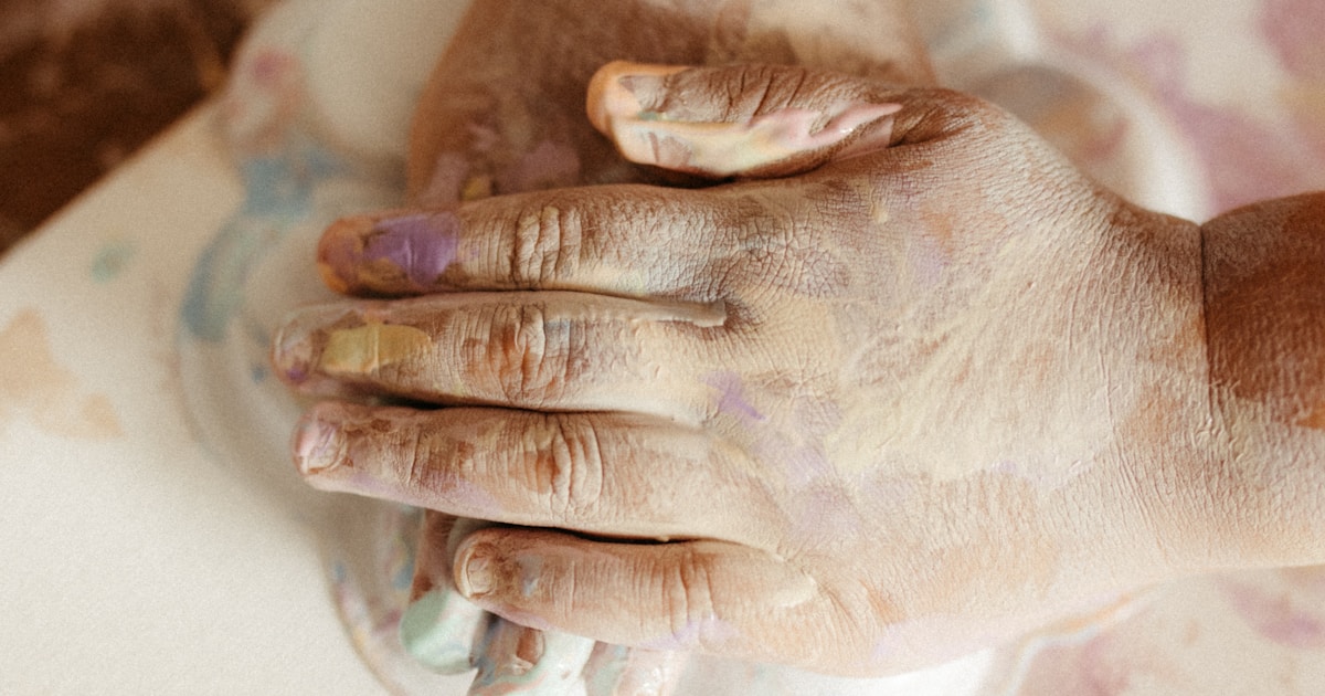 Hands covered in paint mixing colors on canvas