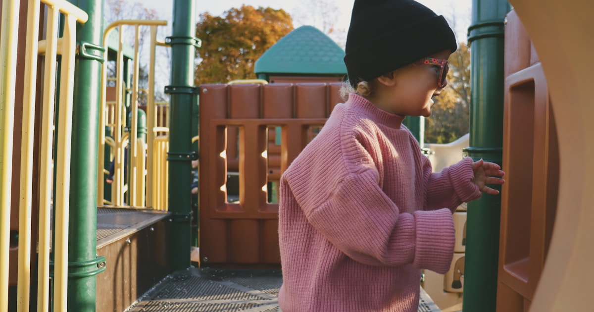 a little girl in a pink sweater playing on a playground