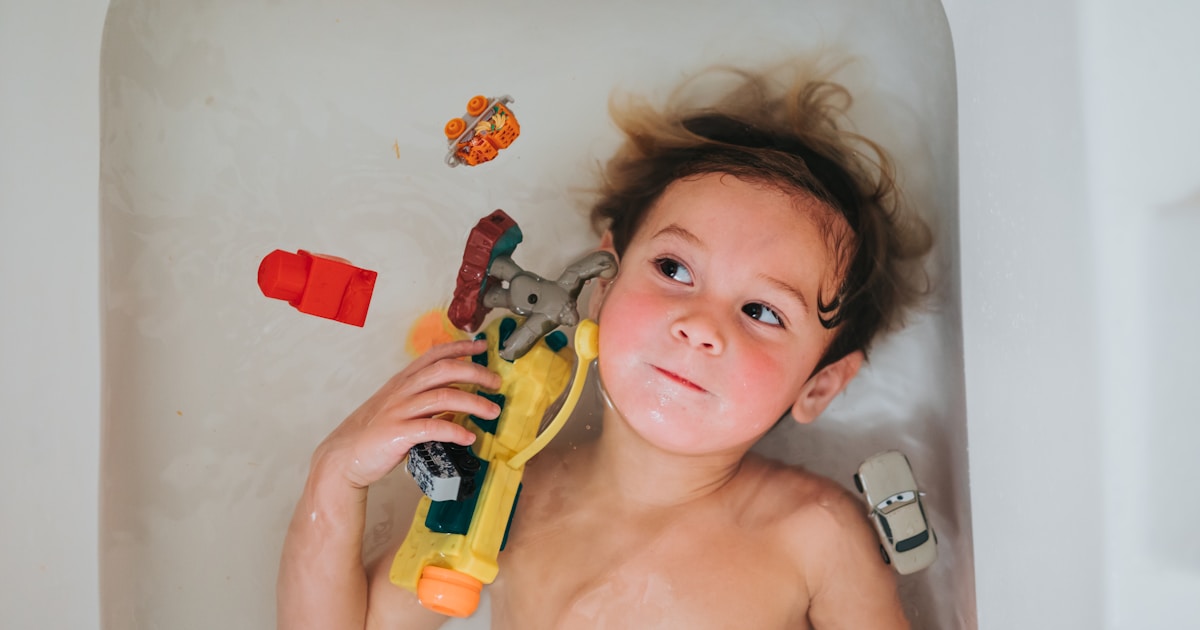 topless baby holding yellow and red plastic toy gun