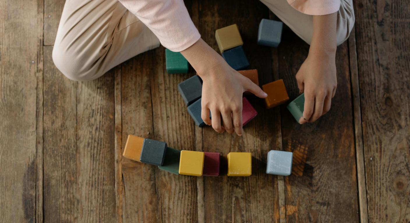 Two small hands arranging colored wooden blocks in a row on a wooden table.
