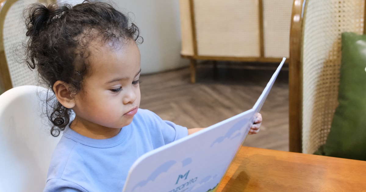 Young child sits in high chair reading a menu.