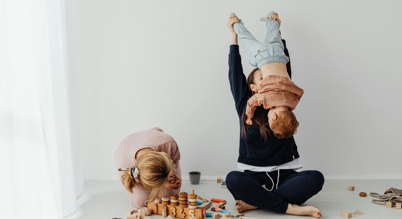 Mother and toddler playing with colorful building blocks on a rug in a living room.