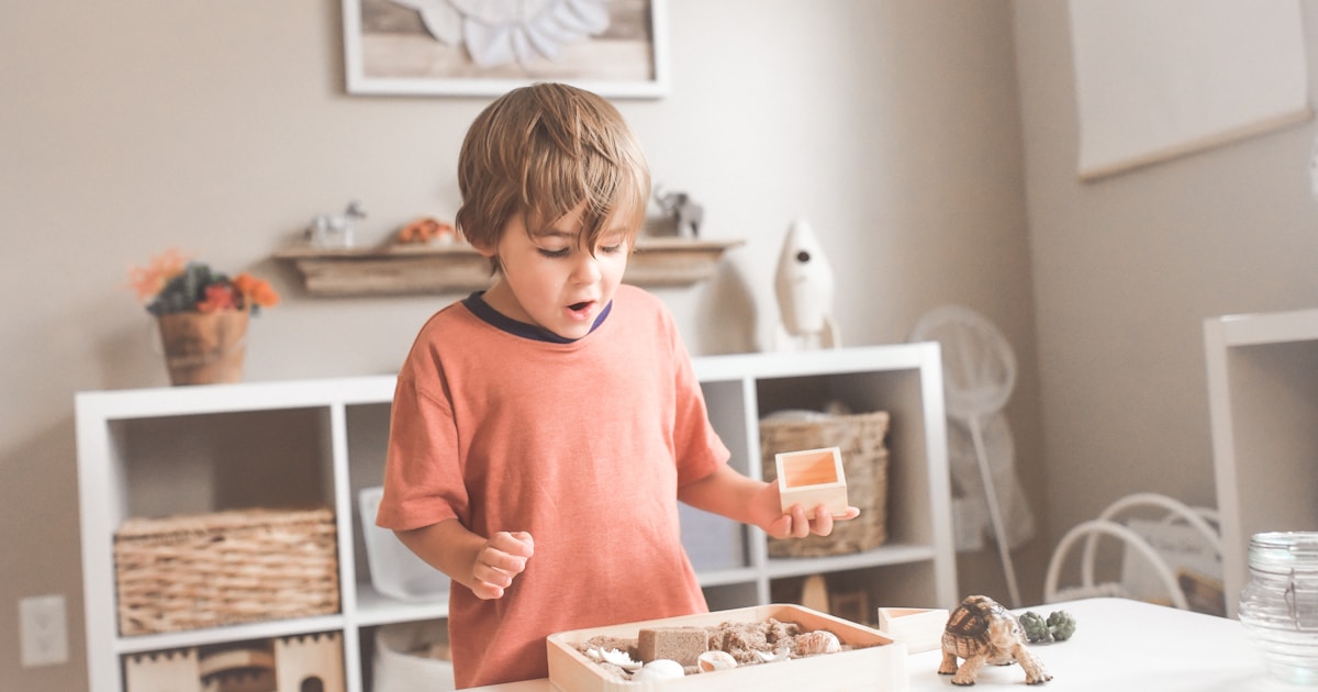 boy in orange crew neck t-shirt standing in front of white wooden table with cupcakes