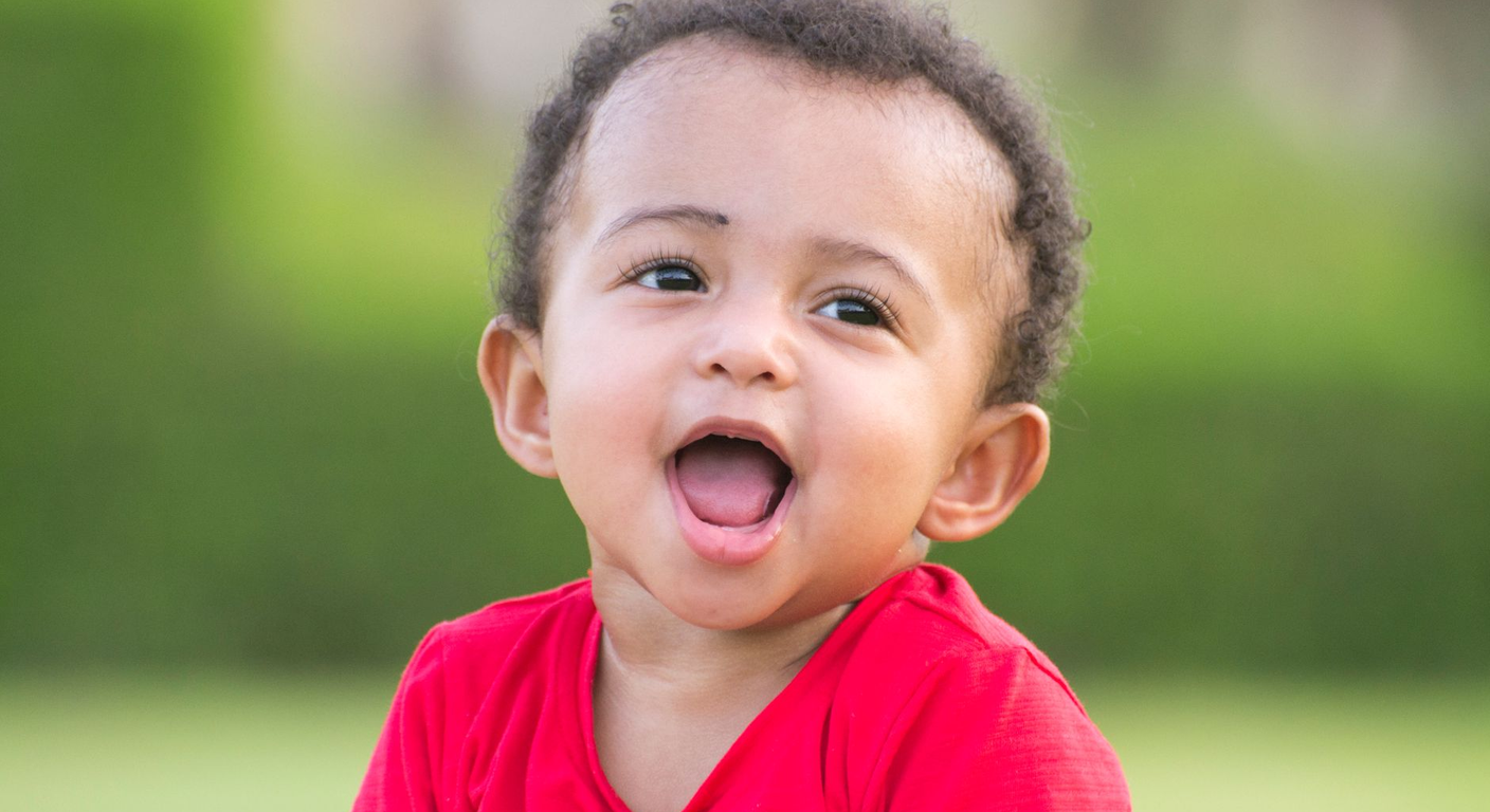 A cheerful toddler outdoors laughing with mouth wide open